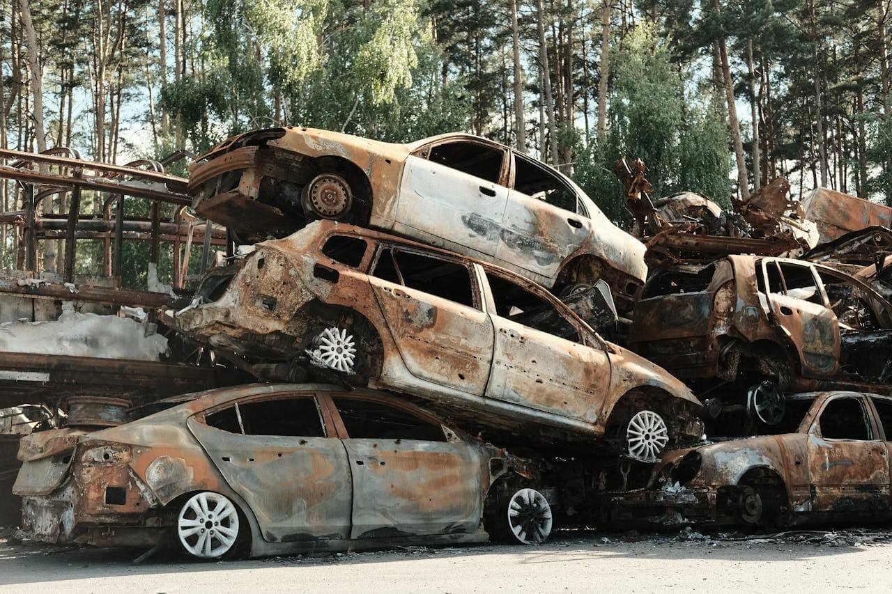 Pile de voitures détruites rouillées dans une casse extérieure entourée d'arbres.